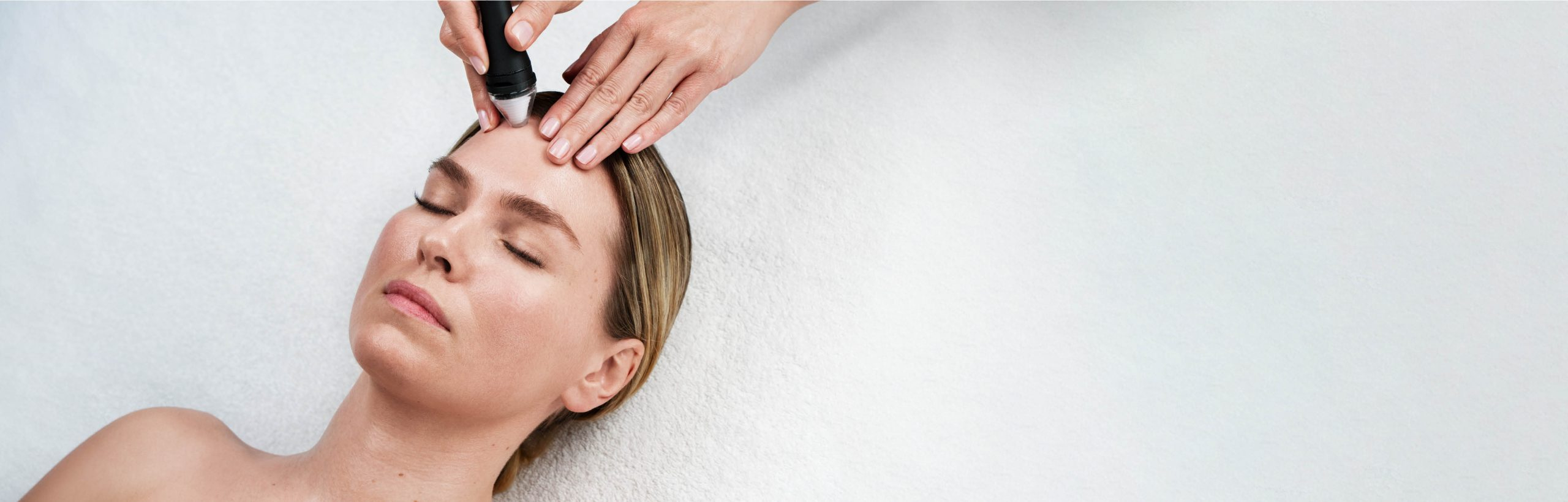 Frau mit geschlossenen Augen, liegend bei einer Gesichtsbehandlung mit Apparat.